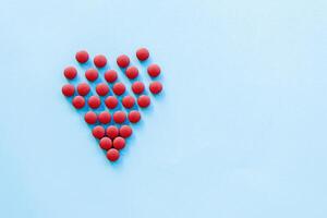 abstract on the topic of a healthy heart, heart disease and the like. bright red pills in the shape of a heart on a bright blue plain background photo