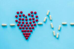 abstract on the topic of a healthy heart, heart disease and the like. bright red pills in the shape of a heart on a bright blue plain background photo