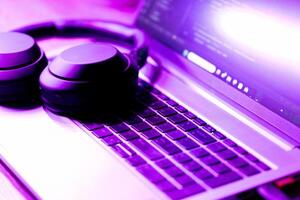 modern wireless headphones and laptop with software code on screen in neon purple light, suitable for software development , IT education topics photo