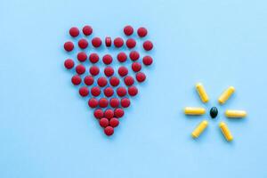 abstract on the topic of a healthy heart, heart disease and the like. bright red pills in the shape of a heart on a bright blue plain background photo