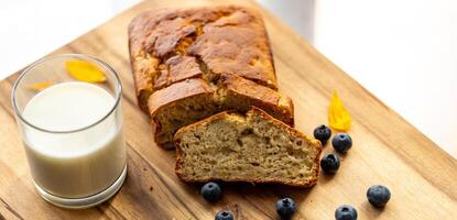 glass of milk and sweet homemade banana bread with crispy crust on a wooden board, dessert photo