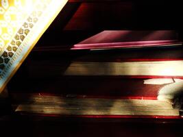 A pile of old hardcover books stored on a wooden shelf in the library covered by yellow and white patterned cloth underneath. The book looked dusty because it had not been touched for a long time photo