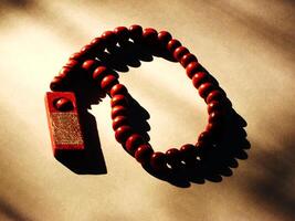 Reddish colored Islamic wooden tasbih isolated on white background. There was yellowish sunlight coming from the side presenting a calm and gentle atmosphere. photo