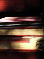 A pile of old hardcover books stored on a wooden shelf in the library. The book looked dusty because it had not been touched for a long time photo