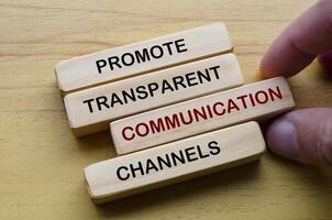 Promote transparent communication channels text on wood block with hand holding one wooden block. Continuous improvement concept photo
