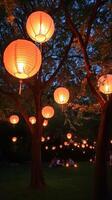 Brightly lit Chinese lanterns hang from trees in night garden. Mid-Autumn festival. Vertical banner photo
