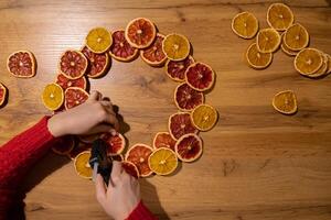 DIY process of woman making Christmas arrangement with dried oranges and grapefruits. Series of handmade craft instruction. Zero waste eco-friendly winter holiday decoration. New year photo