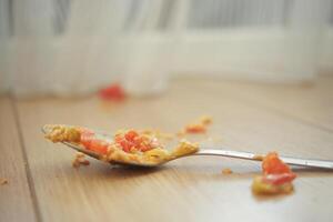 A messy spoon covered in food residue is lying on a wooden floor creating a chaotic scene photo