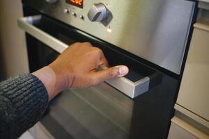 A person is using their hand to open a modern oven, engaging in culinary activities at home photo