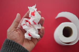 A blood spot is noticeable on a tissue next to a roll of toilet paper in the background photo