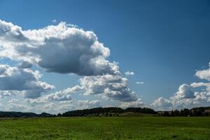 Thick clouds over green fields. The highway is far beyond the field photo