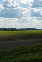 Thick clouds over green fields. The highway is far beyond the field photo