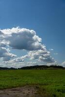 Thick clouds over green fields. The highway is far beyond the field photo