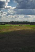 Thick clouds over green fields. The highway is far beyond the field photo