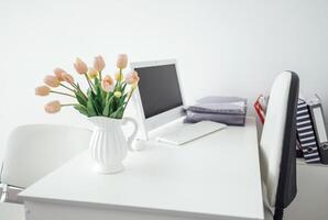 a workplace with a computer, a keyboard, folders with documents and a jug with tulips. Modern stylish interior. photo