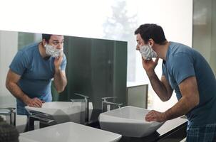 Handsome brunette man shaving in the bathroom. He stands and looks at the mirror with concentration photo