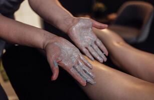 Close up of the masseuse palms with a grey scrub on them. Massage therapist applying cream to the female client legs. photo