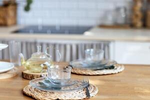Close-up of transparent cups and a teapot with green tea on a wooden kitchen table. Cozy cute room interior. Glassware on wicker stands. photo
