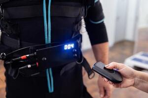 Using the remote control. Trainer sets the necessary parameters on black ems suit for male client. photo