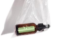 Brown essence or serum glass bottle with a dropper is in transparent plastic bag. Mockup with green sticker on bottle on white background. photo