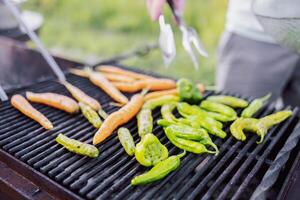 Close-up of a vegetarian barbecue and a cooking man. Tasty fried peppers and carrots on the grill. Vegetables are cooked on coals on the bars in the open air. photo