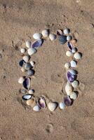 Number 0 laid out from seashells on the sand. Marine background. The symbol is zero. Shells. Copy space. photo