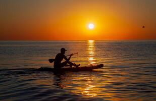 Silhouette of a man floating on a board with an oar. Dawn sun on the sea. Swimming on a supboard. Water active sports. Beautiful landscape. Sunset on the sea. Ocean coast. Copy space. photo