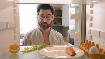 Hungry man guy open empty refrigerator with half lemon lettuce leaf one egg slice of bread leftover orange juice in bottle confused puzzled sad need food delivery point of view POV from inside fridge photo