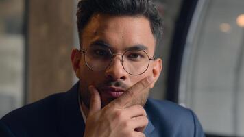 Pensive guy Arabian Indian business man thinking looking at camera close up male thoughtful puzzled businessman office think question idea solution problem search choose decide consider ponder serious photo