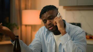 Drunk alcoholism addicted African American man guy male drinking alcohol drink beer at home evening talking mobile phone call smartphone talk speak suffering problem trouble sad upset stress depress photo
