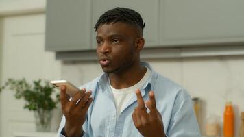 African American man serious biracial male hold smartphone using speaker phone speaking talk to cellphone loudspeaker comfort usage counting with fingers guy record voice message voicemail at kitchen photo
