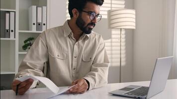 Focused man Arabian Indian ethnic businessman male employee manager writing notes business tasks data paperwork signing documents write on papers counting budget working with laptop computer in office photo