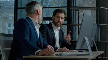 Two Caucasian men professional businessmen work together using computer in office discussing business project check financial data plan colleagues talking about marketing strategy corporate teamwork photo