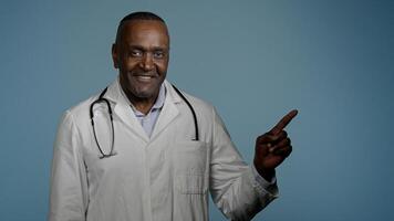 African American man doctor medical worker in white coat male healthcare employee medic customer in studio blue background pointing index finger making choice choosing smiling good selection medicare photo