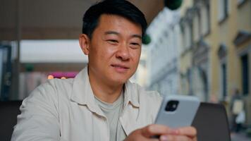 Close-up happy asian man holding mobile phone browsing social network male tourist booking ticket using smartphone sends email message communicates in internet chat making purchase in online store photo