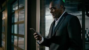 Serious focused businessman holding mobile phone chatting on internet browsing social network mature african man communicate with business client online writing electronic text message uses smartphone photo