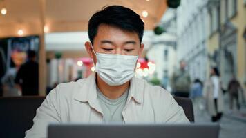 Smiling man in protective mask look at laptop screen chatting remote with friend on social media watching funny sending email asian businessman tourist communicate on internet using computer app photo
