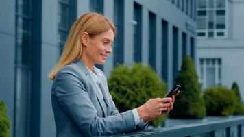 Smiling attractive woman standing outdoors holding phone checking email making order in online store happy businesswoman communicating in social network using mobile app on smartphone browsing media photo