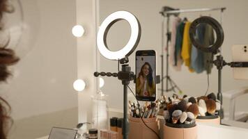 Glad Caucasian woman blogger girl influencer filming mobile phone on stabilizer lamp studio female vlogger streamer talk demonstrating shadow palette do makeup tutorial beauty stream blog mirror photo