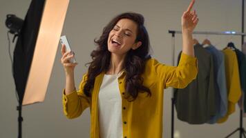 Smiling cheerful Caucasian female woman girl model turning on music mobile smartphone phone dancing fooling around. Positive lady blogger move influencer vlogger singing listen trendy song in studio photo