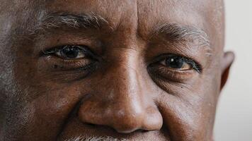 Macro extreme close up half part of face elderly middle-aged African old wrinkled man with dark eyes sad calm mature male senior citizen looking at camera myopia vision sight problem poor eyesight photo