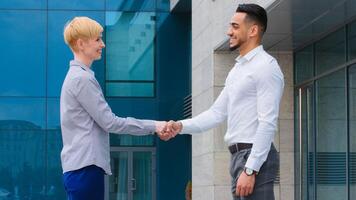 Two multiethnic colleagues arabic man and caucasian woman business partners stand outdoors near company building talking shake hands conclude deal union agreement handshake teamwork goodbye gesture photo