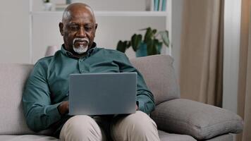African American bald bearded businessman teacher writer entrepreneur checking data online use computer application connection wifi network at home office sitting on comfortable sofa typing on laptop photo