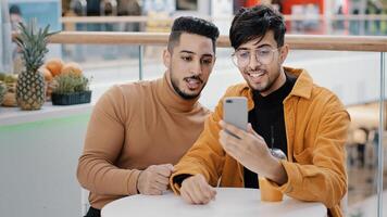 Two happy arab friend bloggers sitting in cafe recording blog on phone communicating via webcam looking at smartphone screen take selfie making videos on social media using mobile application photo