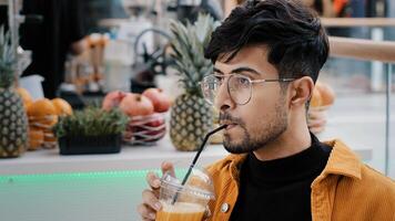 Young hispanic male cafe client resting spending weekend drinking exotic drink from plastic disposable cup relaxing happy carefree guy enjoying taste refreshing fruit juice looking at camera smiling photo