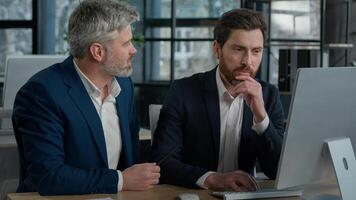 Mature businessman mentoring man discussing project on computer consulting investor client about digital investment in office Caucasian businessmen colleagues working together discuss data management photo