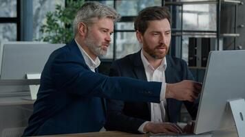 Mature businessman mentoring man discussing project on computer consulting investor client about digital investment in office Caucasian businessmen colleagues working together discuss data management photo