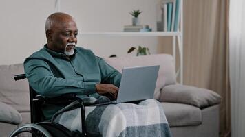 Pensive though in deep thinking. old 60s American businessman sitting at home in wheelchair online working typing on laptop writing text novel report. male writer think about idea use computer net app photo