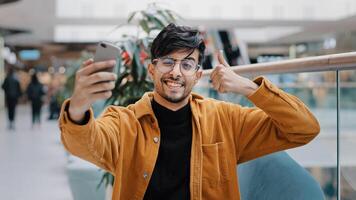Young handsome arab guy blogger model holding phone in hand photographed on mobile camera posing smiling making gesture taking photo filming for blog on smartphone using chat application