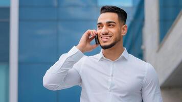 Hispanic indian bearded businessman with mobile phone at street smiling Arabian businessman manager answer call with smartphone outdoors distant communication cheerful guy talking cellphone outside photo